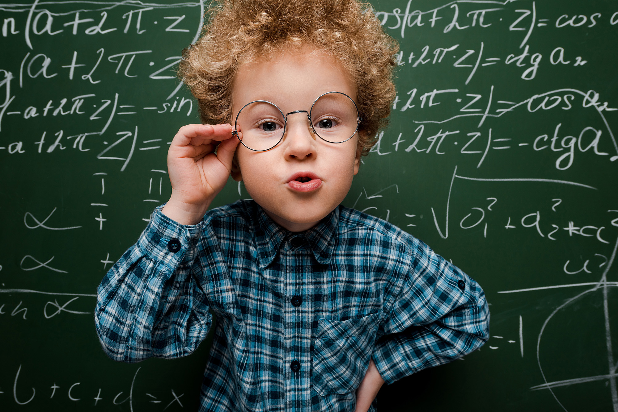 smart kid touching glasses and standing with hand on hip near ch School boy with glasses